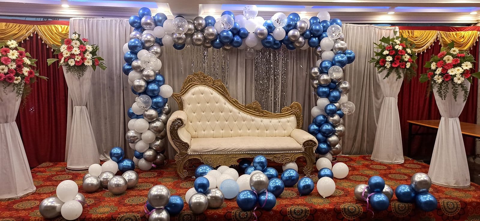 Blue, silver and white balloon arch around a white chaise on a hall stage
