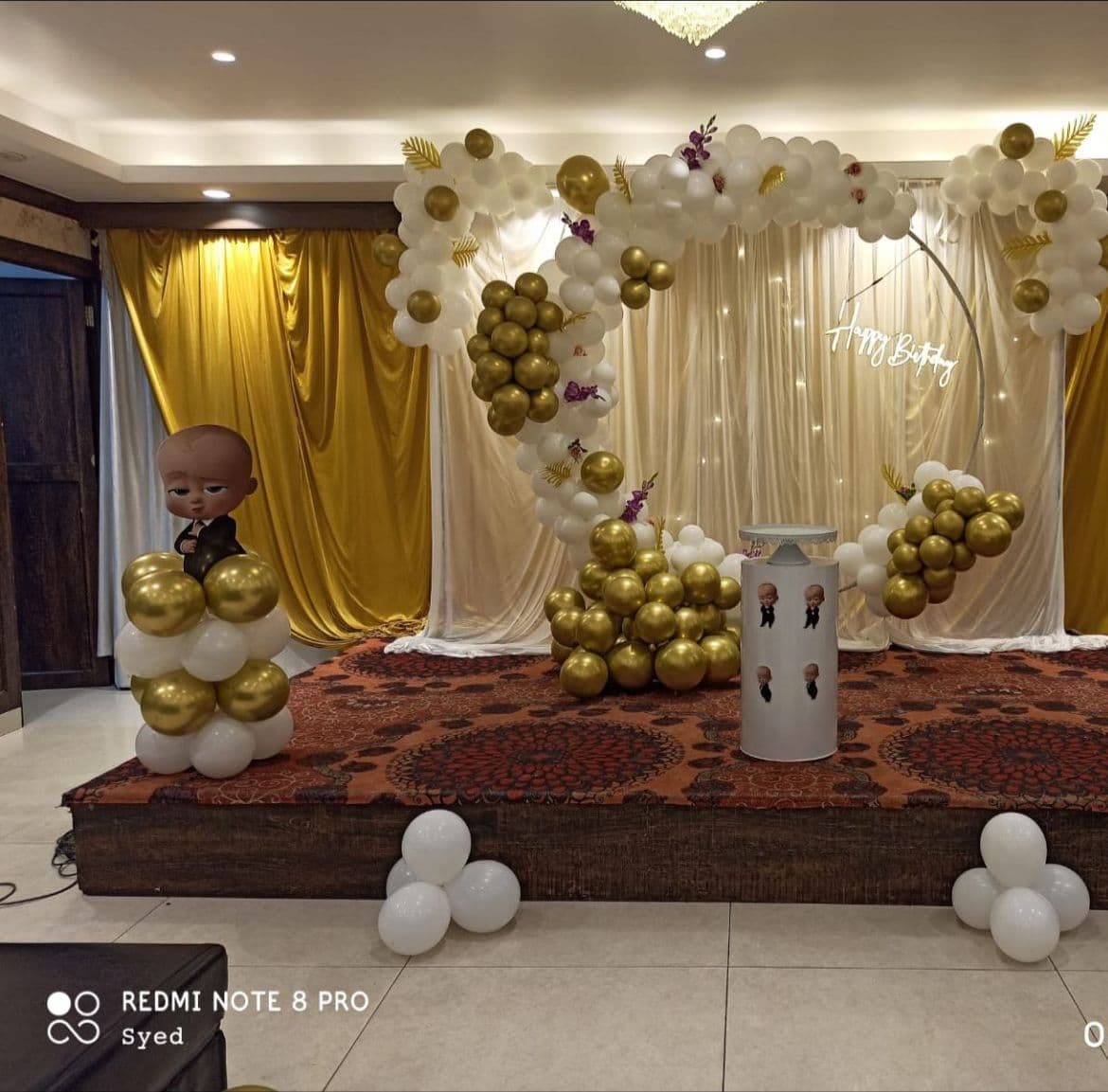 Boss Baby themed birthday stage in gold and white balloons