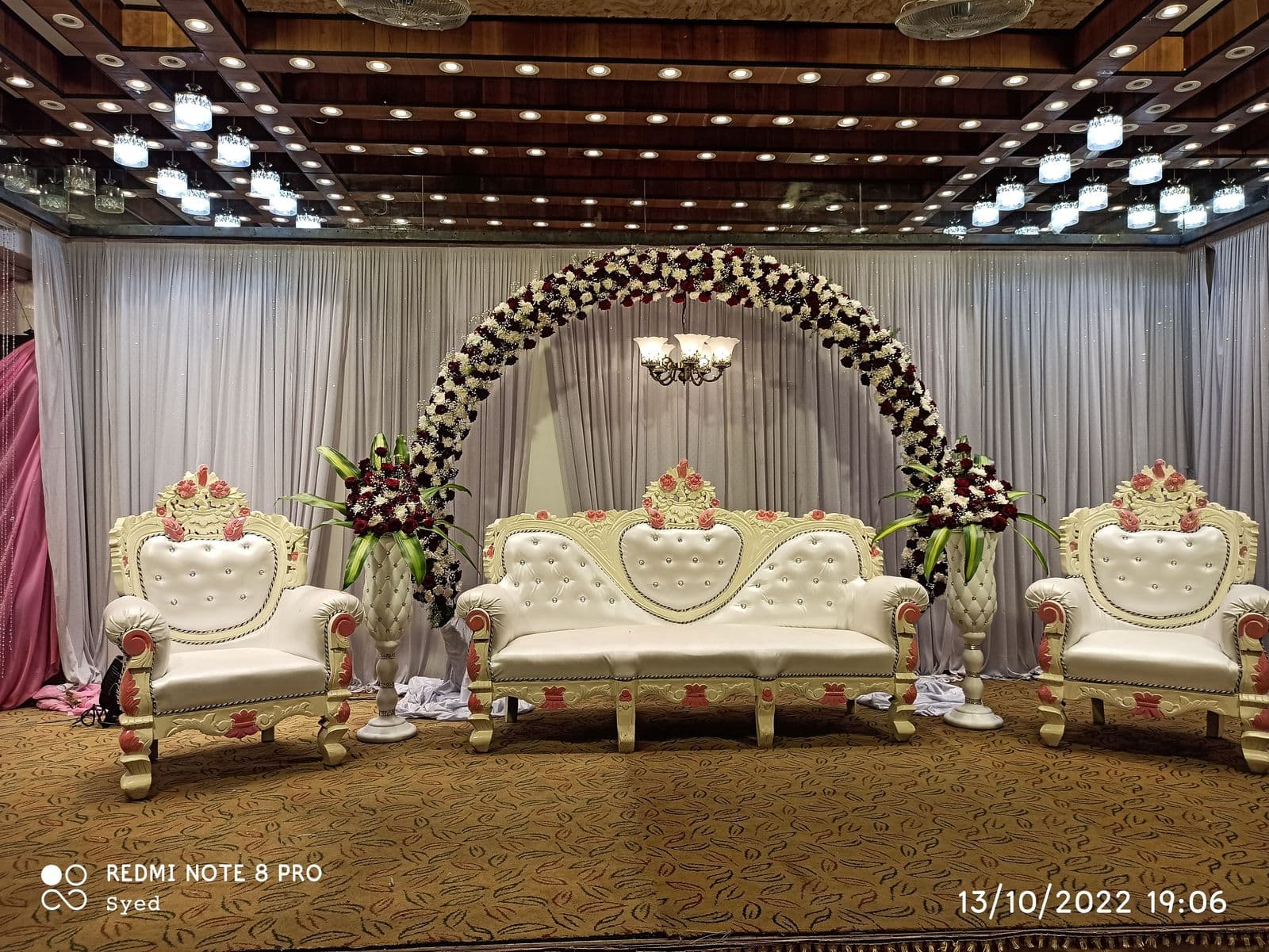 Floral arch stage with white sofas for the couple and family