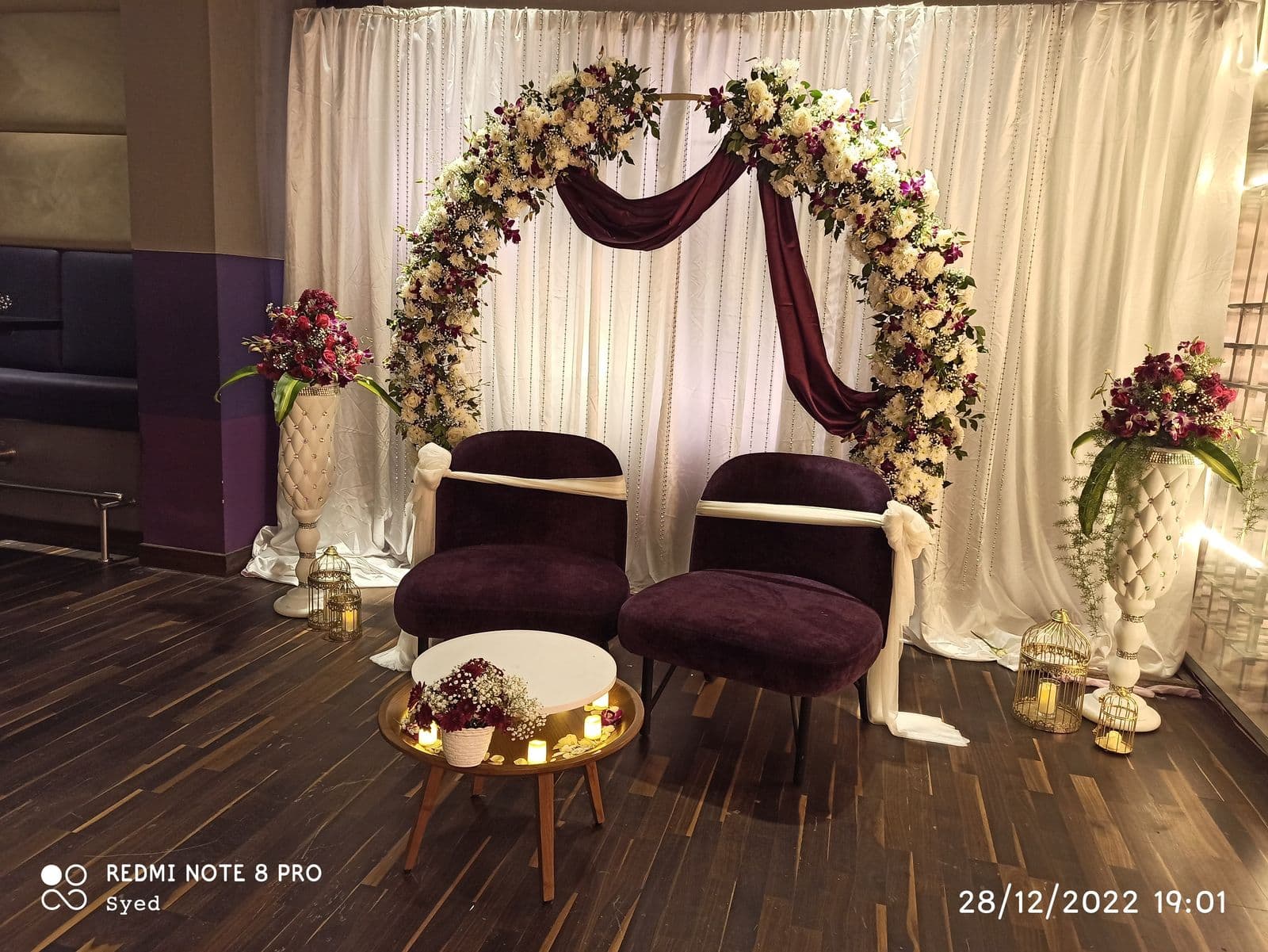 Floral ring with maroon swag and velvet chairs for a couple