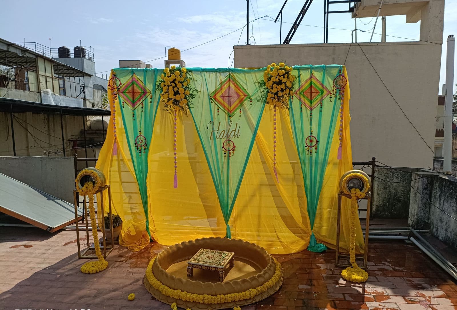 Rooftop haldi setup with green and yellow drapes and a flower urli