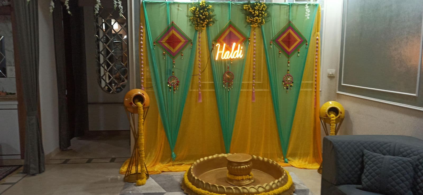 Haldi backdrop in green and yellow triangles with Haldi sign and brass urli