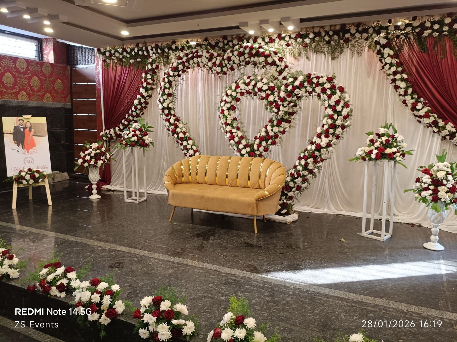 Engagement stage with floral heart rings, maroon drapes and a gold sofa