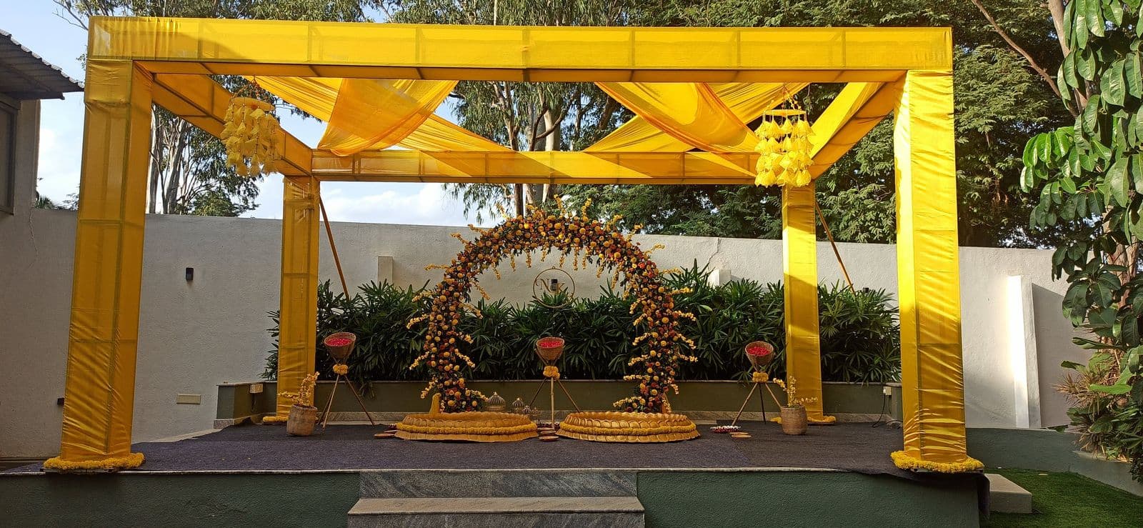 Outdoor haldi pergola in yellow drapes with floral ring