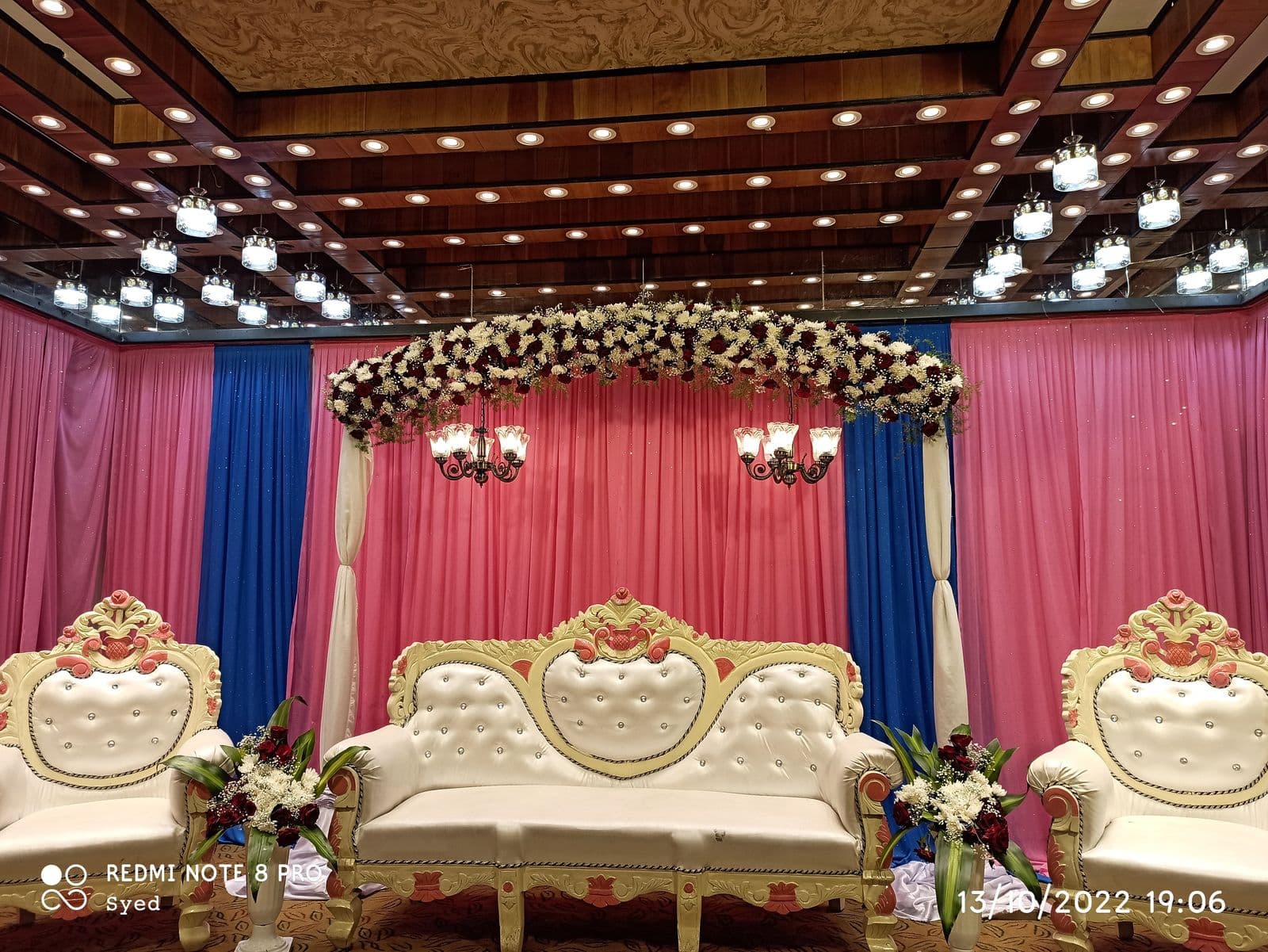 Pink and blue drape stage with floral arch and white sofas