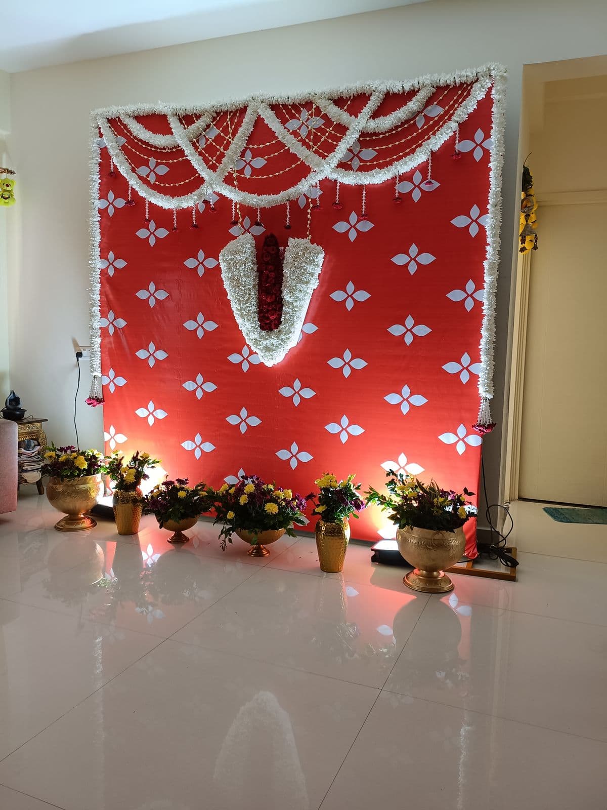 Red pooja backdrop with white garland and brass lamps