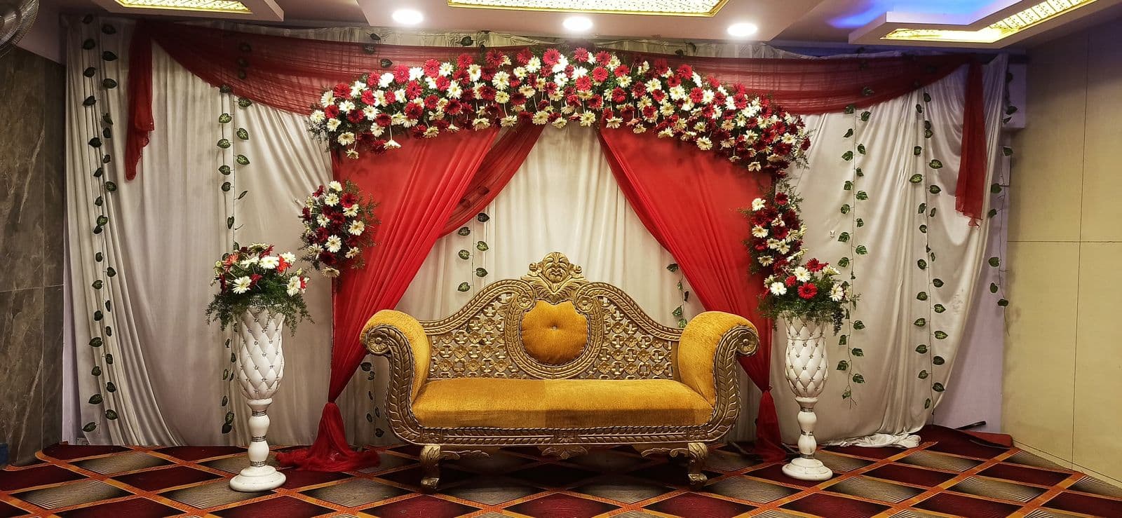 Red and white drape stage with floral arch and gold sofa