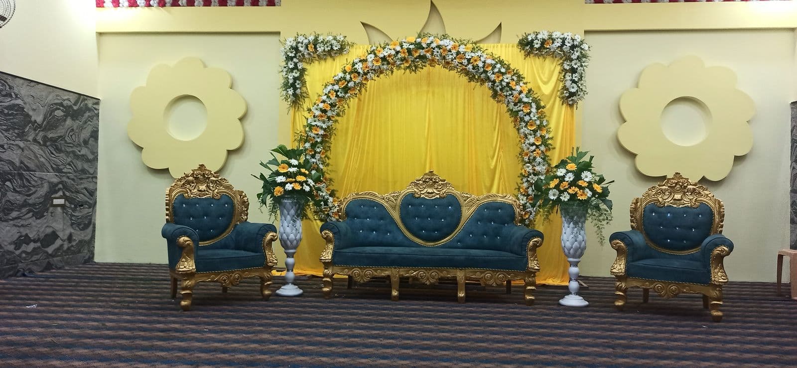 Yellow backdrop stage with floral arch and blue sofas