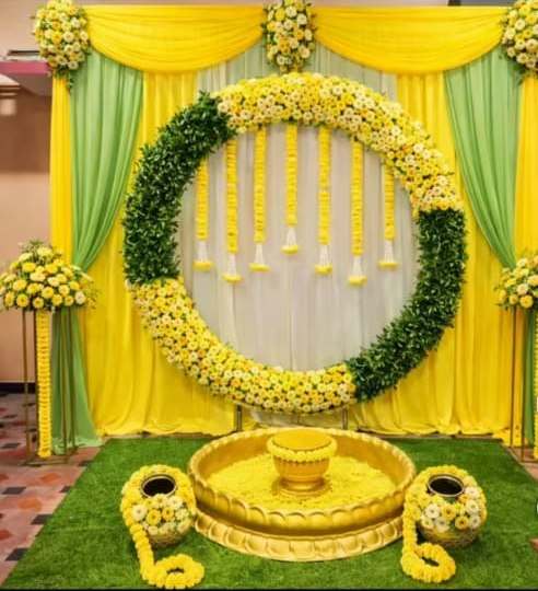 Circular floral ring haldi backdrop with green and yellow drape swags and gold urli