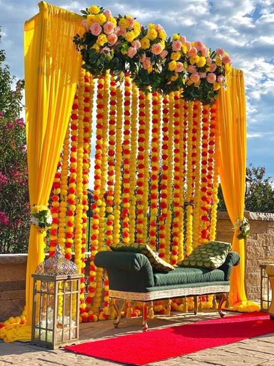 Outdoor haldi seating with marigold and rose garland curtain and yellow drapes